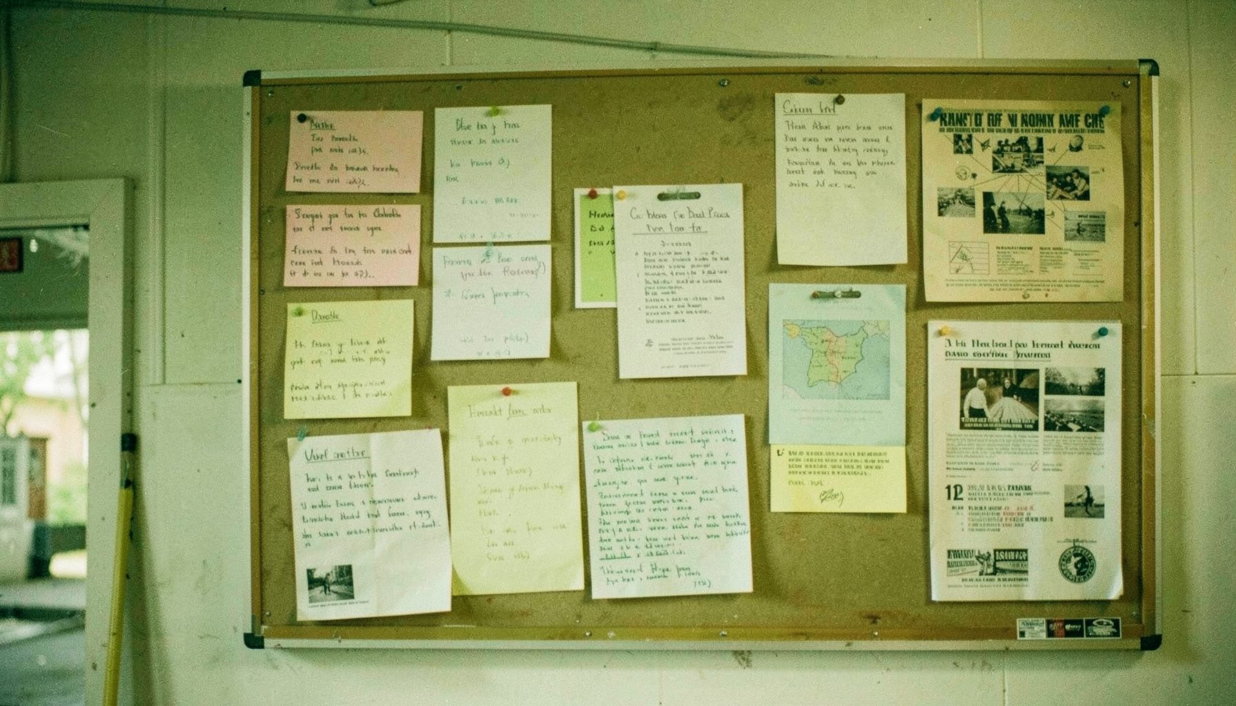 A softly lit community bulletin board with pinned notes and flyers in warm cream and olive tones, conveying a sense of quiet, ongoing community activity.